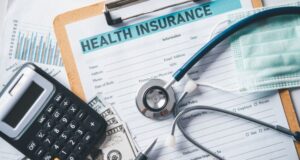 Imagem de uma caderneta com um formulario de Health Insurance, calculadora, dinheiro, uma mascara e um estetoscopio